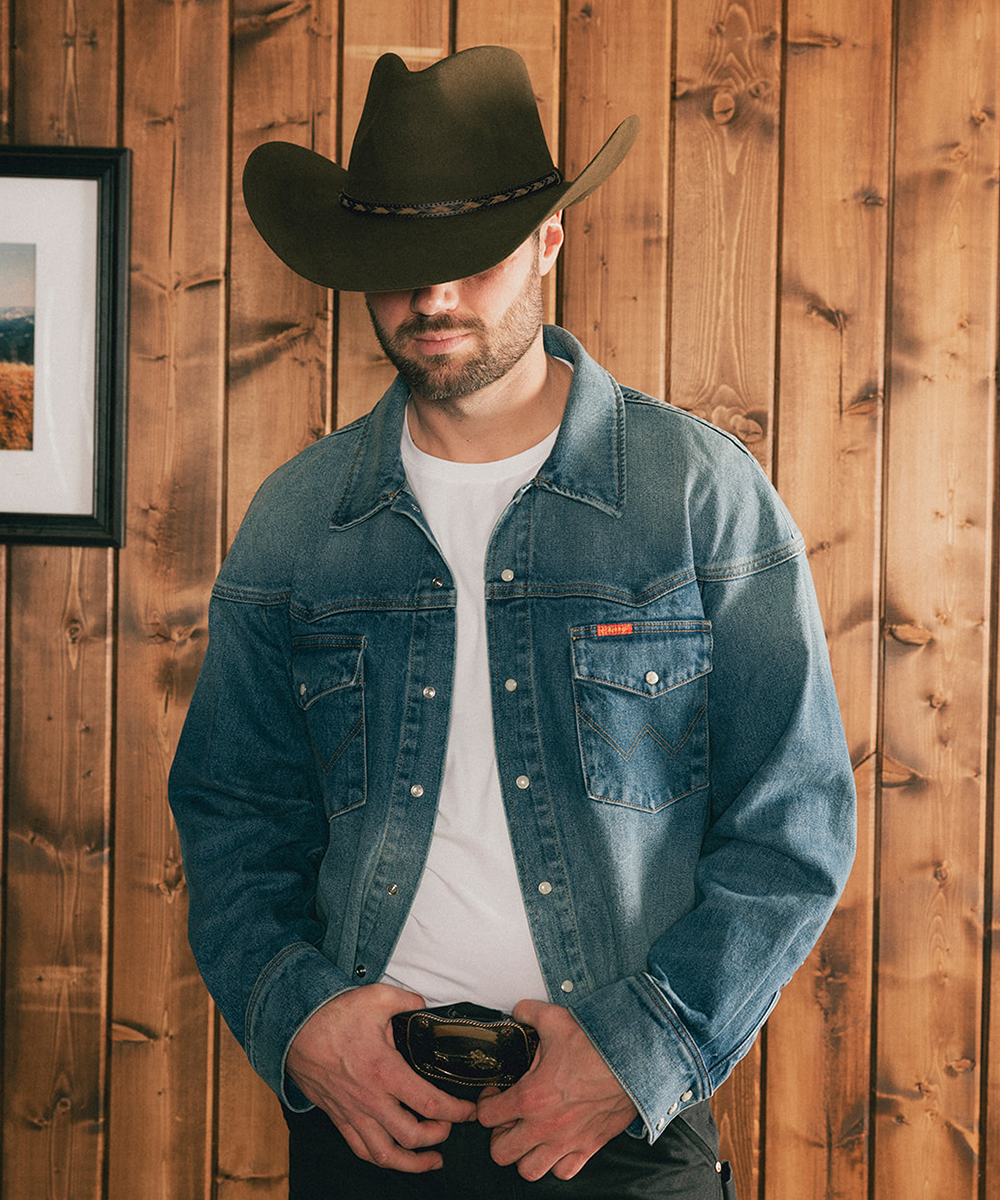Man wearing a denim jacket and cowboy hat against a wooden wall #color_moss
