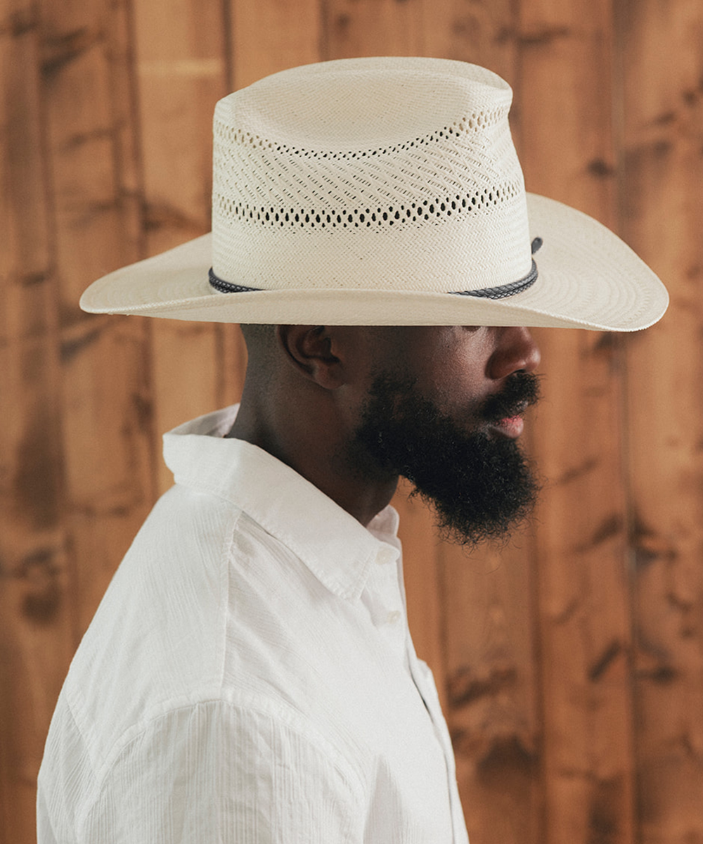 Man wearing a white cowboy hat and white shirt against a wooden background #color_ivory