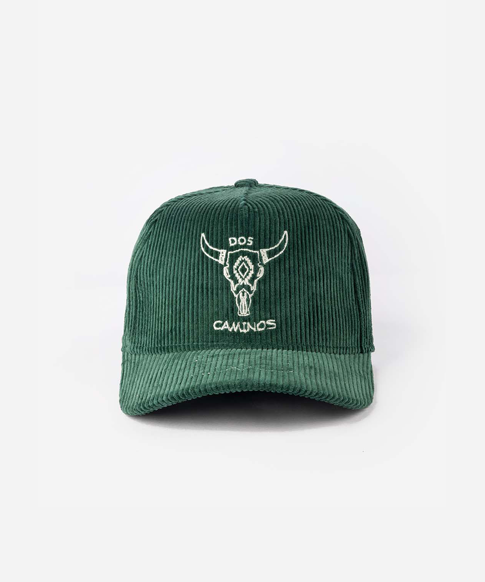 A dark green corduroy baseball cap with a white embroidered bull skull logo and the text 'DOS CAMINOS' on the front, set against a plain white background #color_saguaro