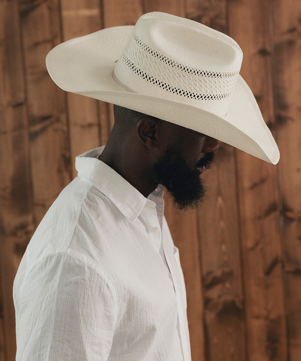 Man wearing a wide-brimmed white hat against a wooden background #color_ivory