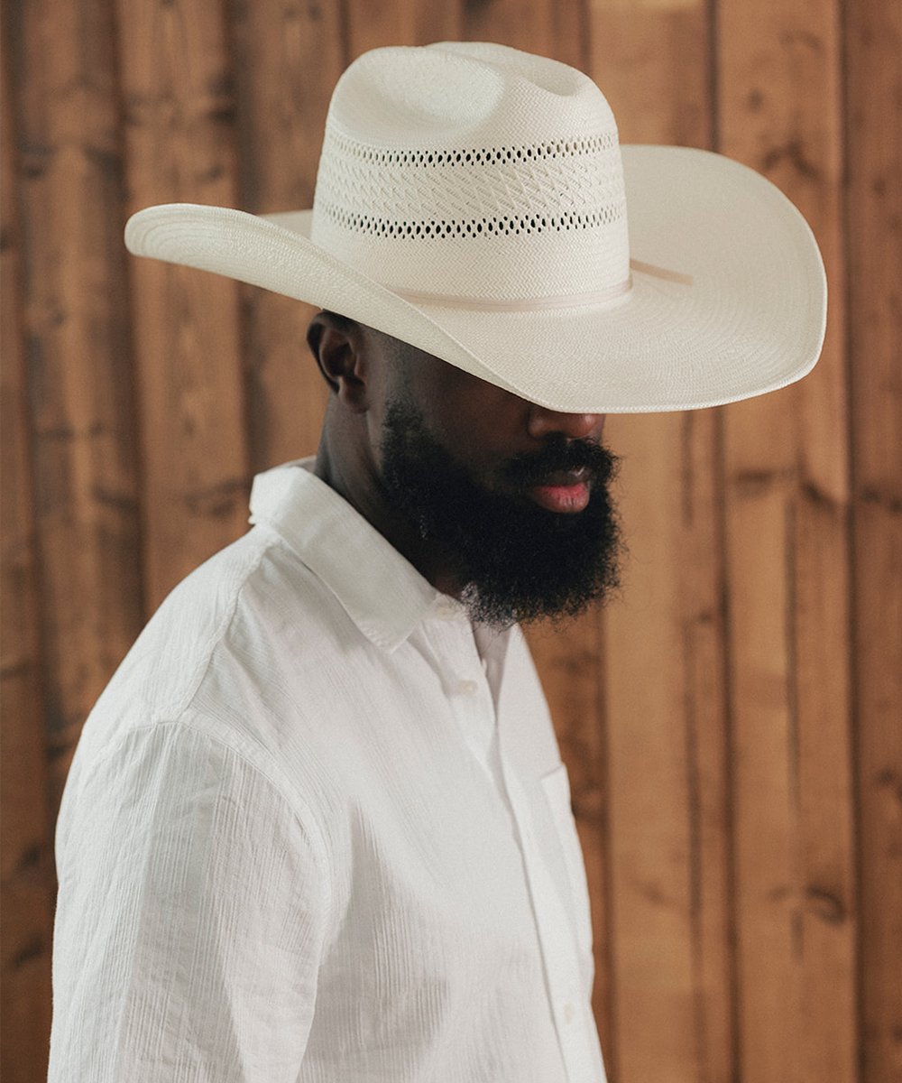 Man wearing a wide-brimmed white hat against a wooden background #color_ivory
