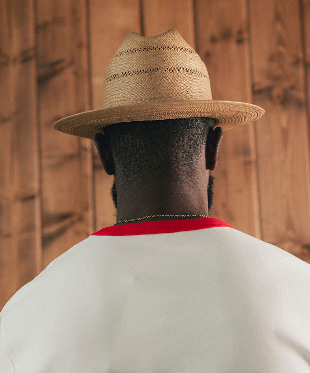 Man sitting on a stool in a room with wooden paneling, wearing a white shirt with red trim and blue jeans #color_natural