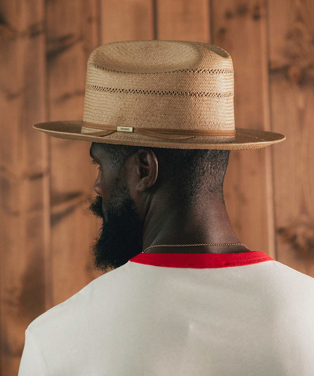 Man sitting on a stool in a room with wooden paneling, wearing a white shirt with red trim and blue jeans #color_natural