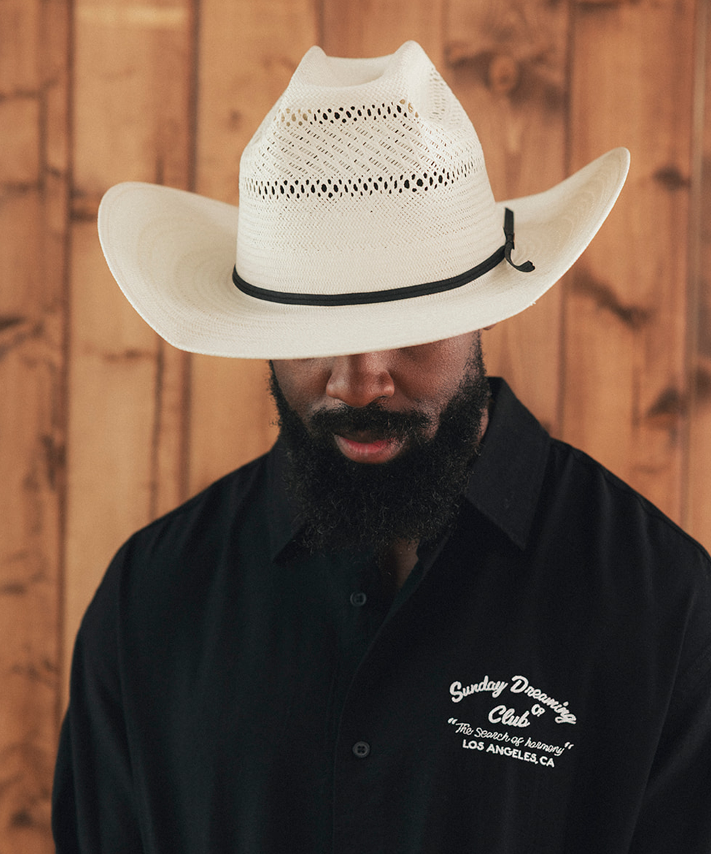 Man wearing a white cowboy hat and black shirt with text against a wooden background #color_ivory