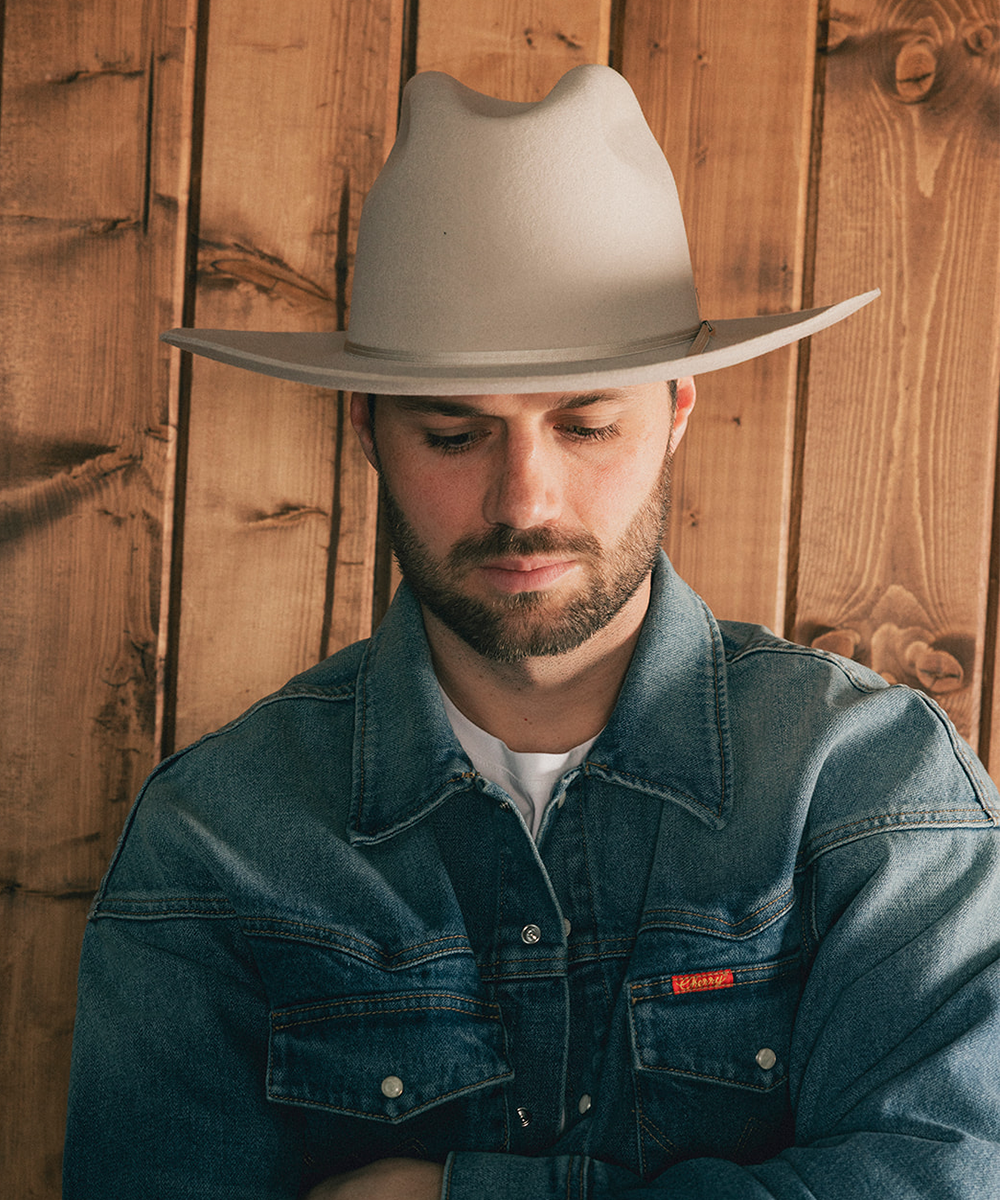 Man wearing a beige cowboy hat and denim jacket against a wooden background #color_silverbelly