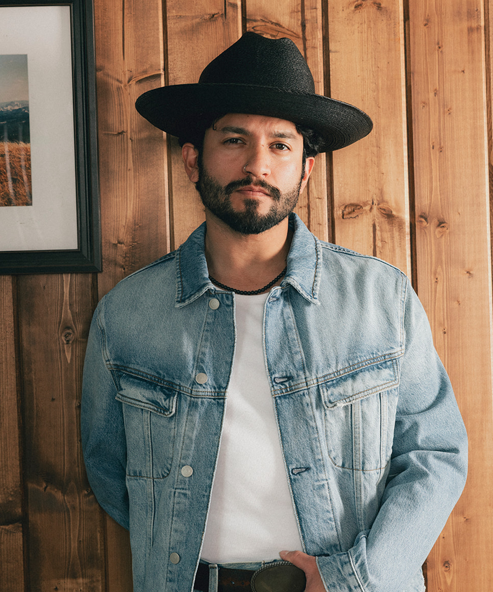 Man wearing a black straw hat and denim jacket against a wooden wall #color_black