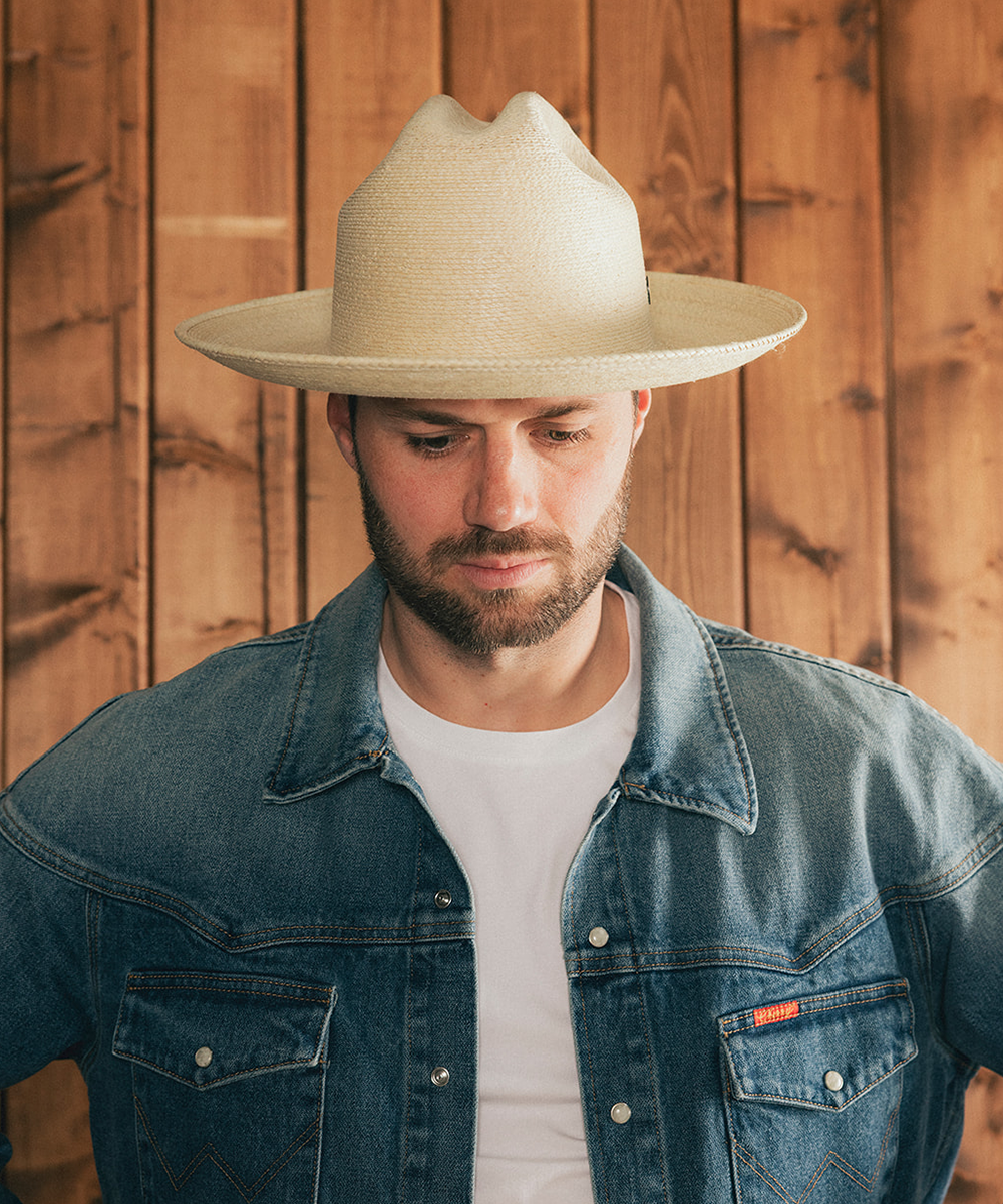 Man wearing an ivory straw hat and denim jacket against a wooden background #color_ivory